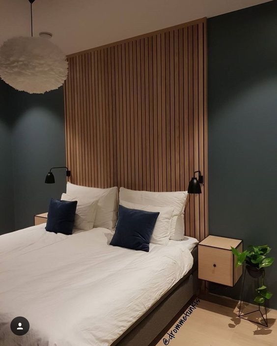 a bed with white sheets and blue pillows in a room that has wooden slats on the wall