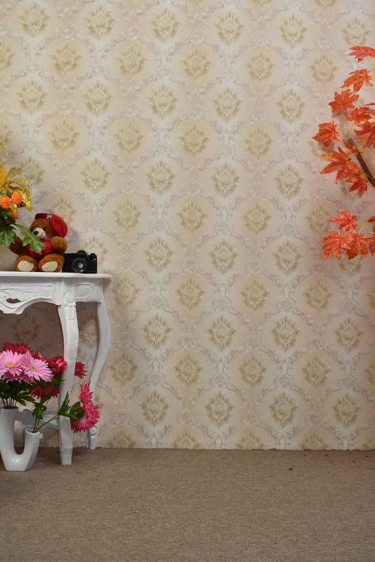 a small white table with flowers on it next to a wallpapered background and a potted plant