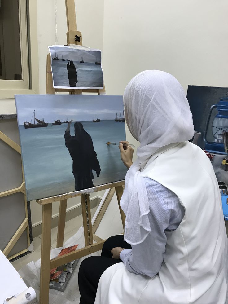 a woman sitting in front of an easel painting