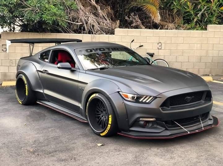 a gray mustang with yellow rims parked in a parking lot