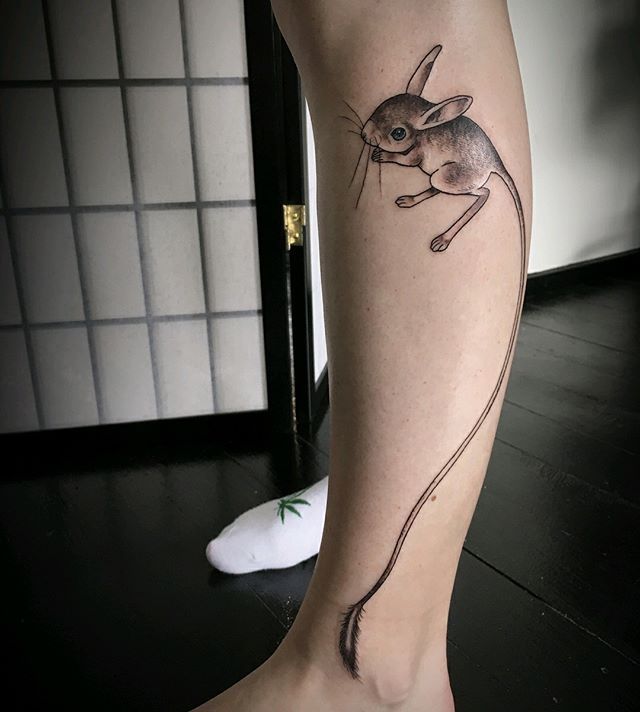 a tattoo on the leg of a woman with a mouse in it's mouth