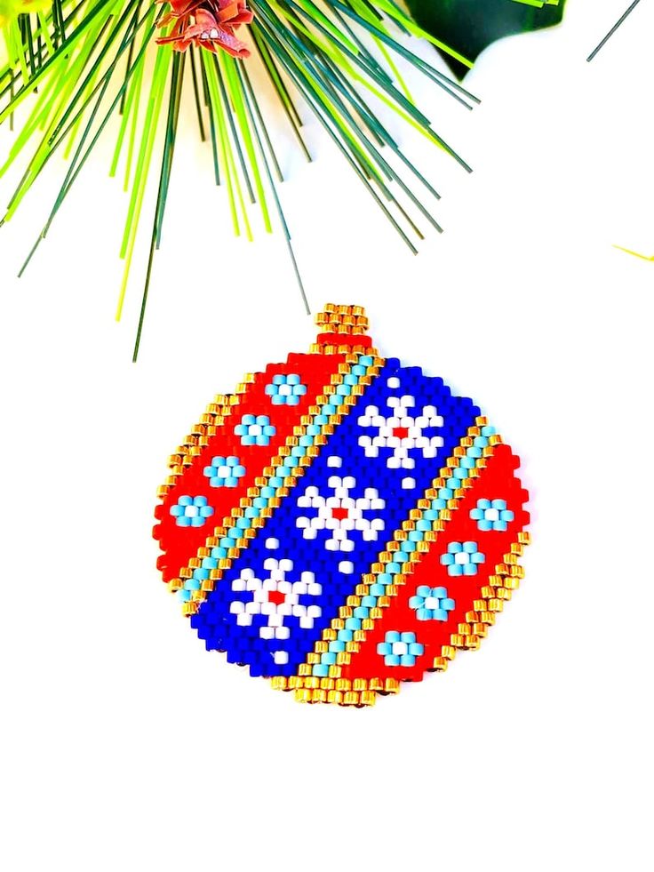 a beaded ornament hanging from a pine tree branch on a white background