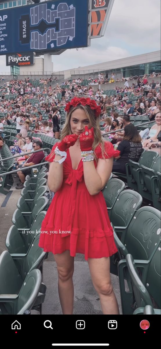 a woman in a red dress and gloves at a baseball game with her hands on her face