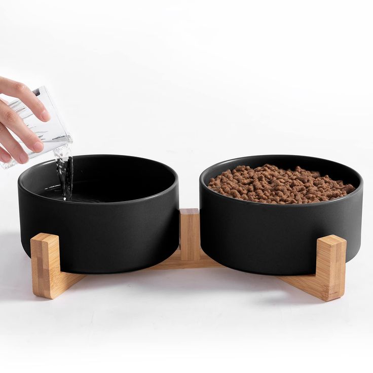 a person is pouring water into two black bowls with food in them on a wooden stand