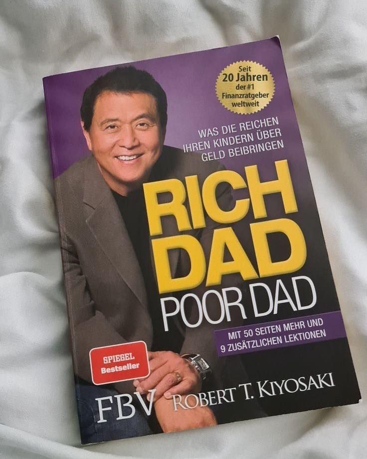 the book rich dad poor dad is laying on a bed