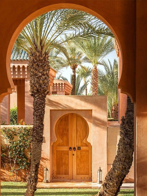 an archway leading to a building with palm trees in the foreground and grass on the ground