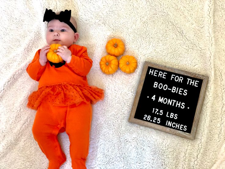 a baby in an orange outfit laying next to a sign that says here for the boo - bibs 4 months