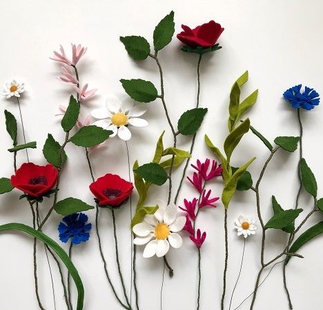 several different colored flowers with green stems on a white surface and one red flower in the middle