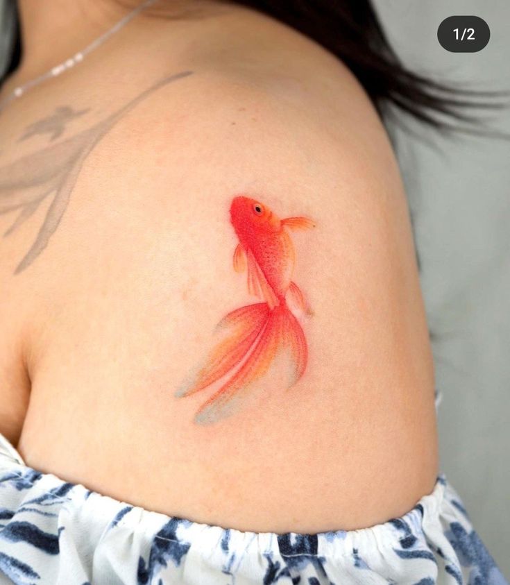 a woman's shoulder with a goldfish tattoo on it