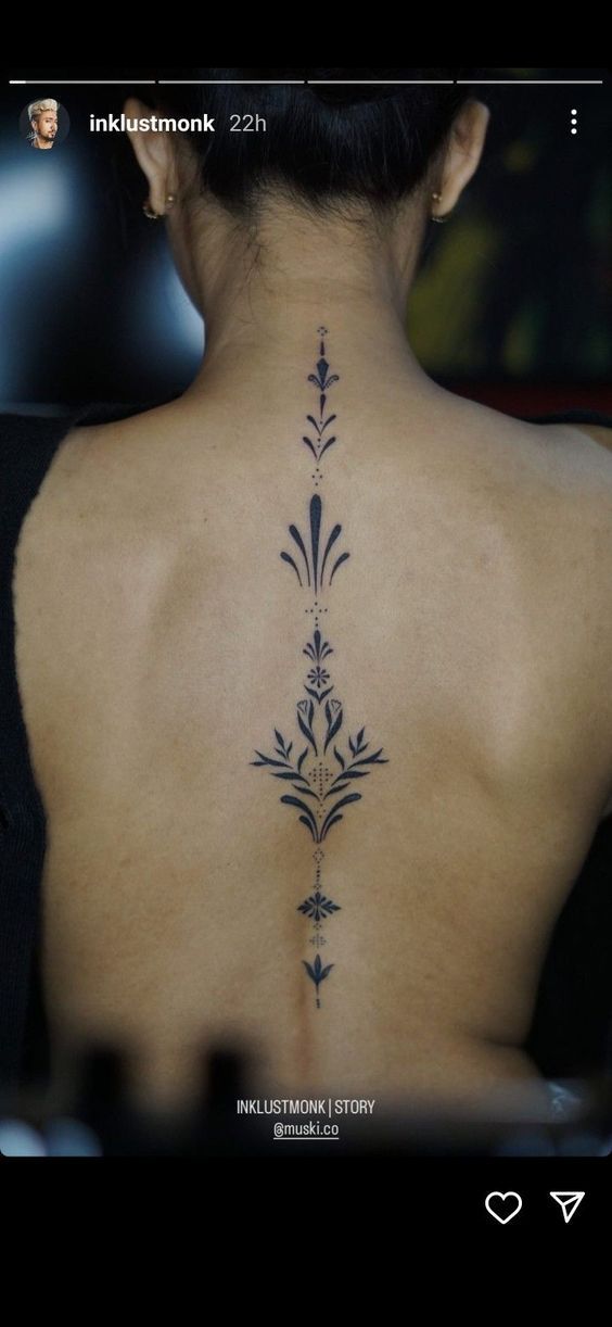 the back of a woman's neck with an intricate tattoo design on her lower back