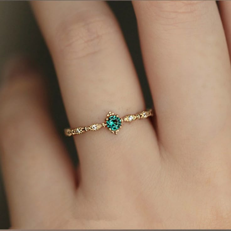 a woman's hand with a ring on it that has a green stone in the middle