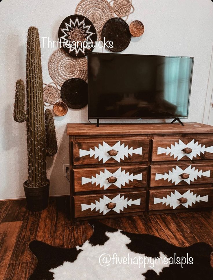 a flat screen tv sitting on top of a wooden dresser next to a cacti