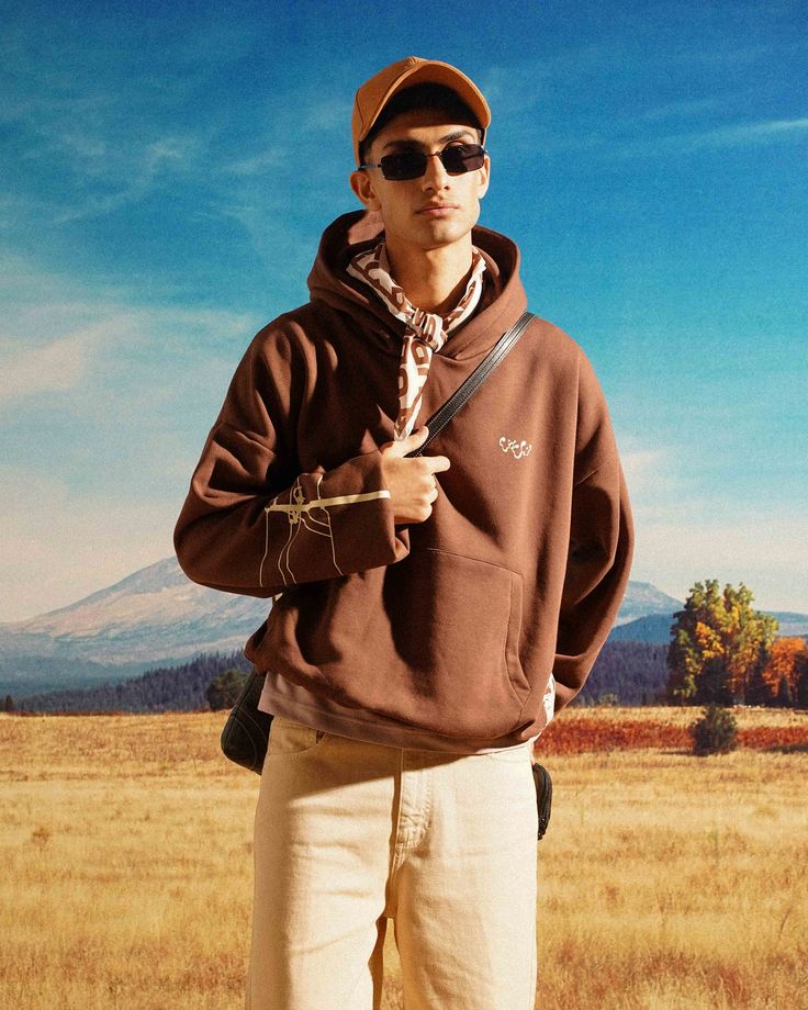 a man standing in the middle of a field wearing sunglasses and a hoodie, holding a pair of scissors