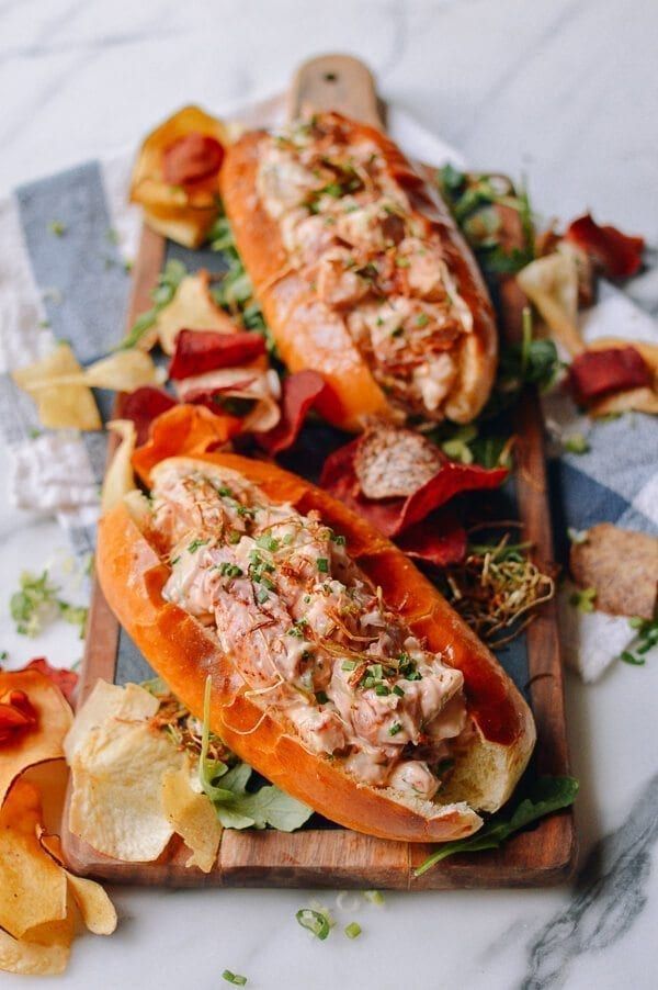 two hot dogs with toppings and chips on a cutting board