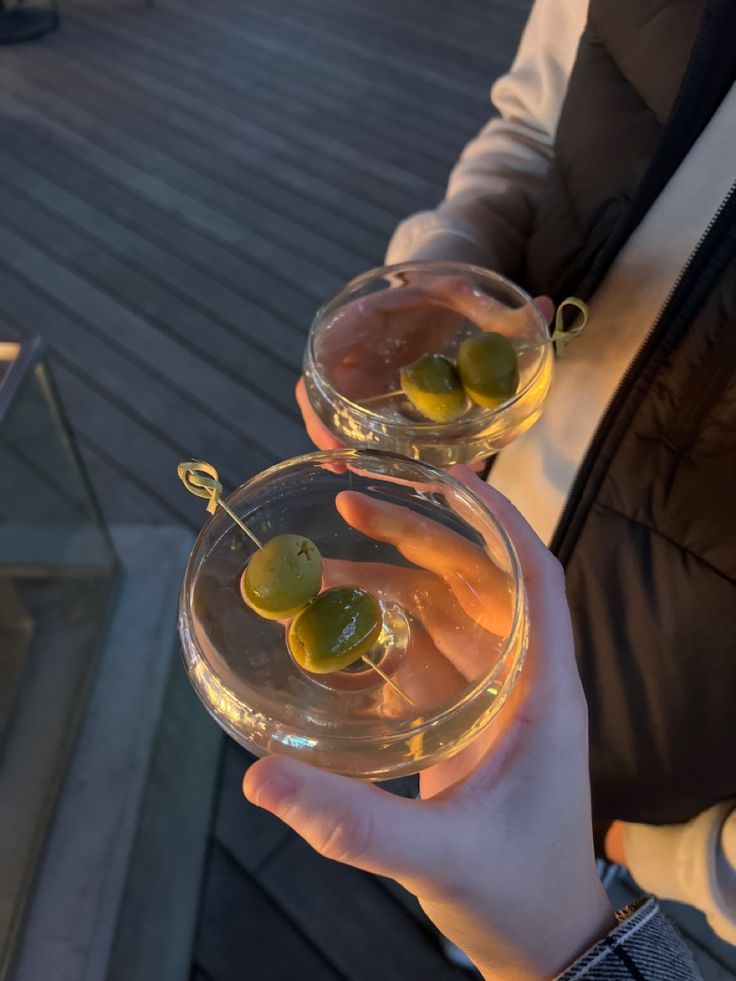 two people holding wine glasses with olives in them