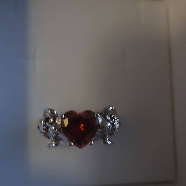 a red heart shaped diamond ring sitting on top of a table