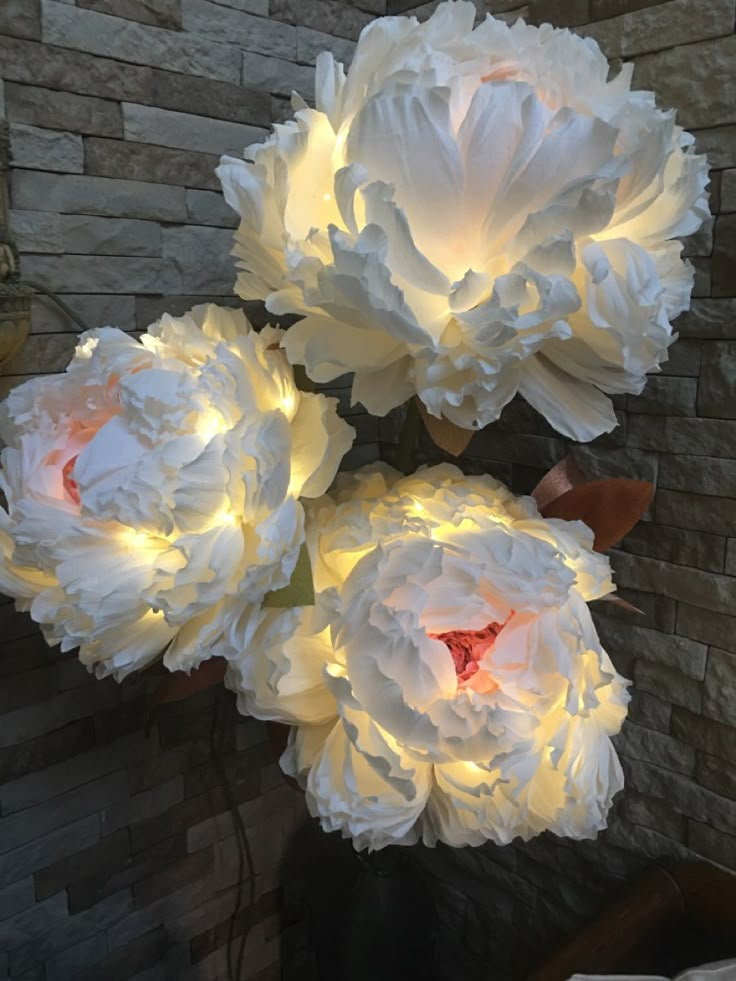 three large white flowers are lit up in front of a brick wall