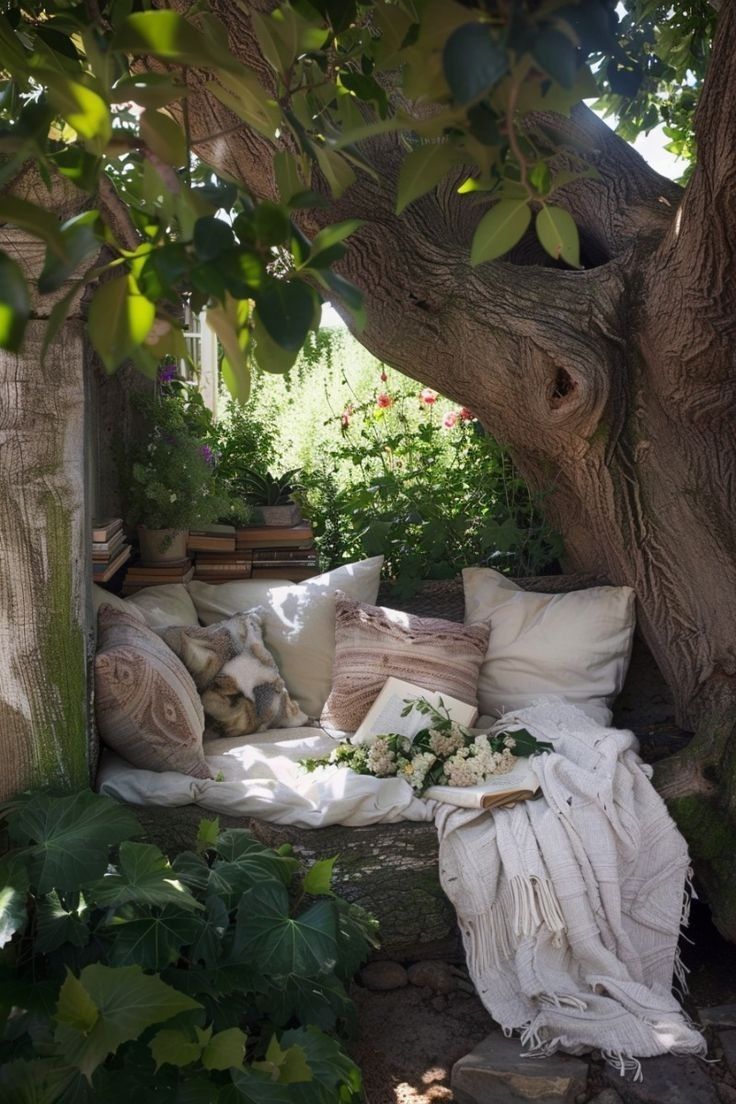 an outdoor seating area under a tree with lots of pillows and blankets on the ground