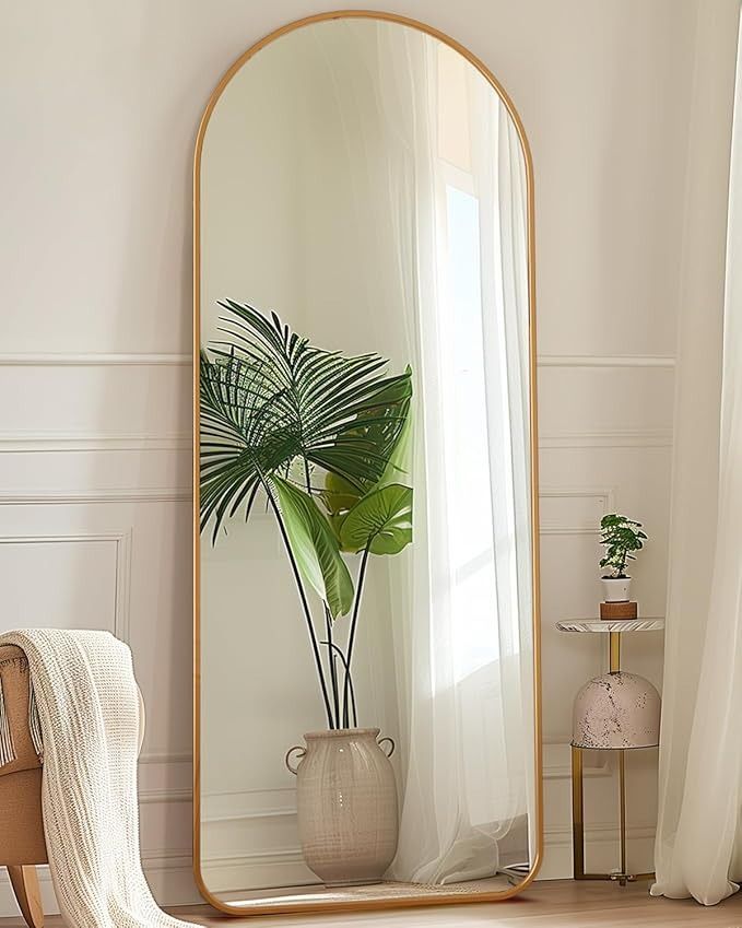 a large mirror sitting on top of a wooden floor next to a plant in a vase