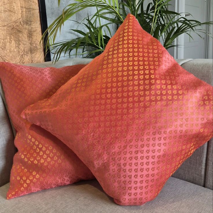 two orange pillows sitting on top of a gray couch next to a potted plant