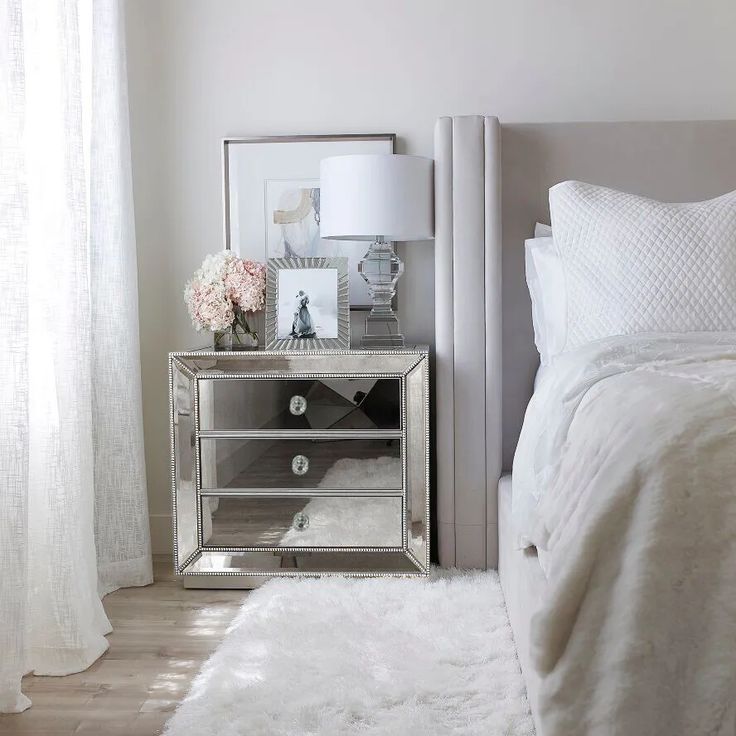 a bedroom with a mirrored nightstand and white fur rug on the floor next to it