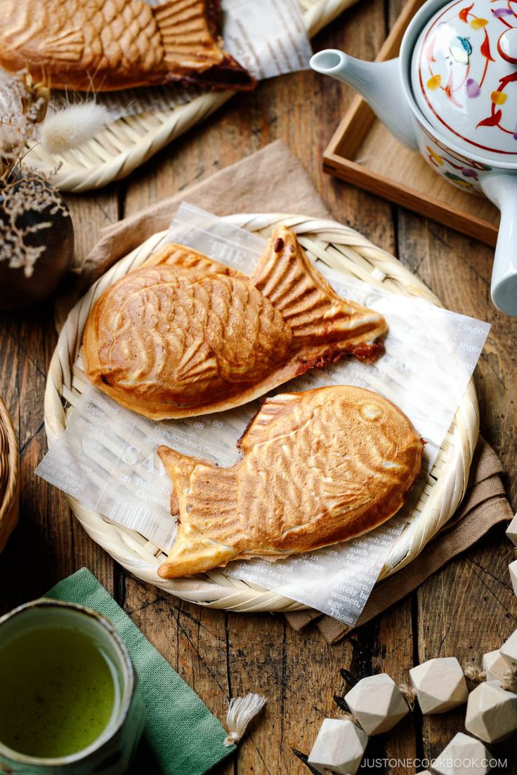 two fish shaped pastries sitting on top of a wooden table next to cups and saucers