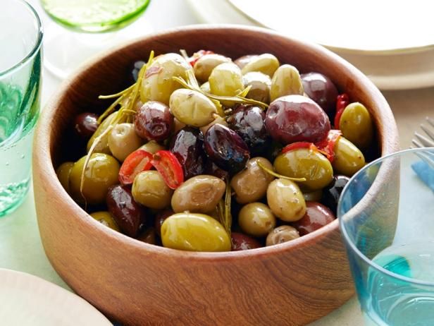 a wooden bowl filled with olives on top of a table next to plates and glasses