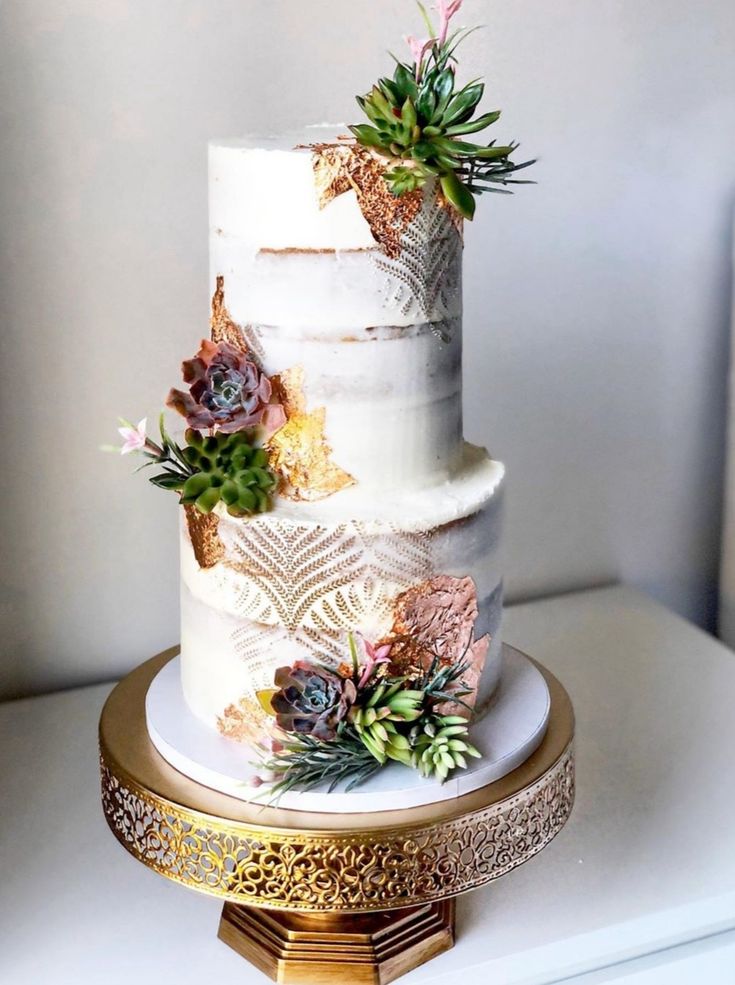 a three tiered white cake with succulents on top and gold trim