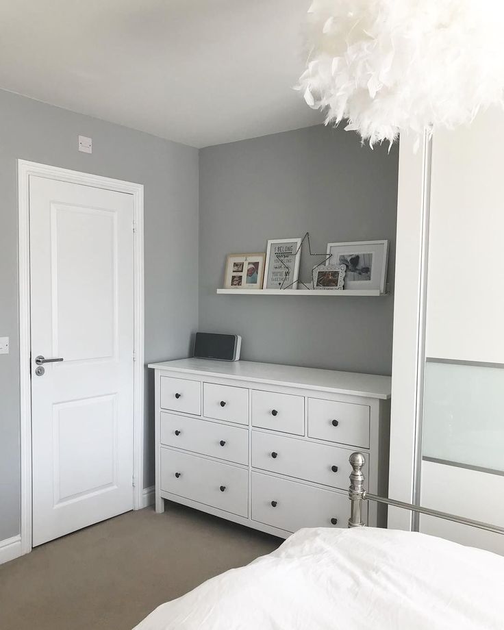 a bedroom with gray walls and white dressers in the corner next to a bed