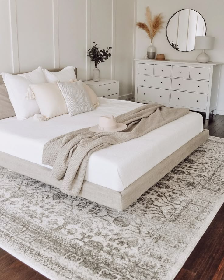 a large bed sitting on top of a wooden floor next to a white dresser and mirror