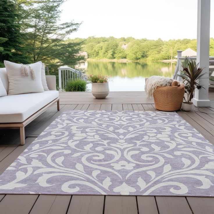 a large rug on a wooden deck with white furniture and trees in the background,