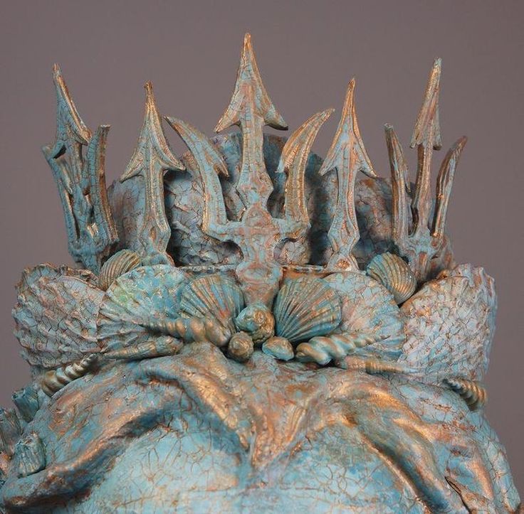 a blue sculpture with many different designs on it's face and hands, sitting in front of a gray background