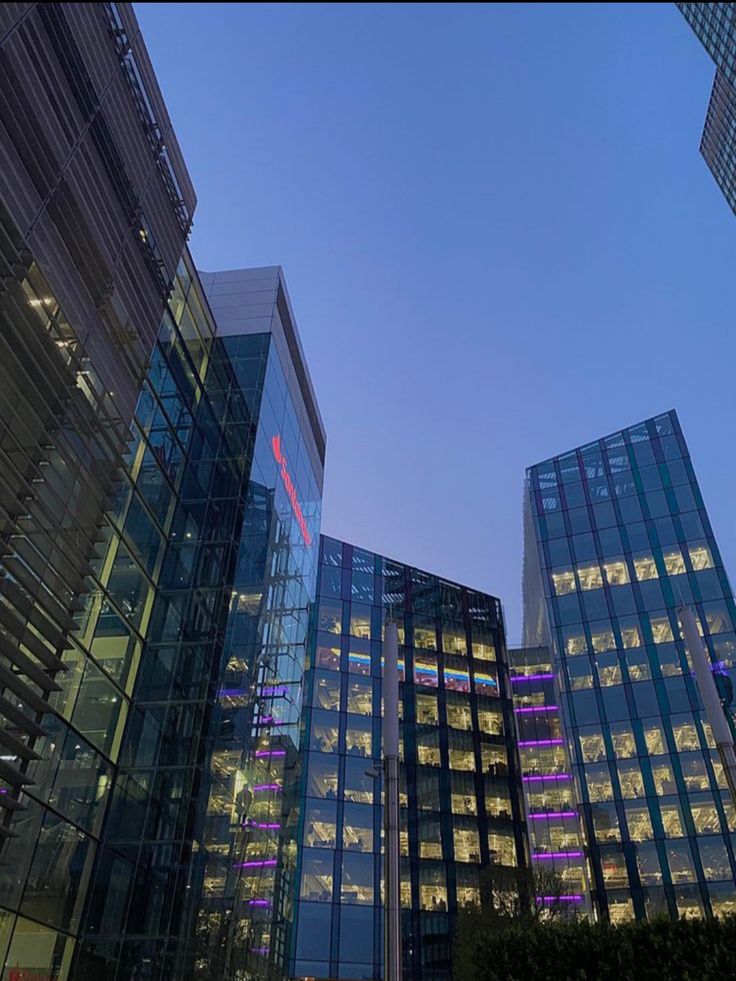 some very tall glass buildings with lights on them at dusk or dawn in the city