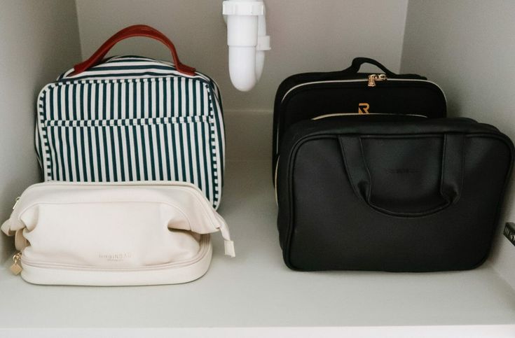 three bags sitting on top of a white shelf next to a toothbrush and other items