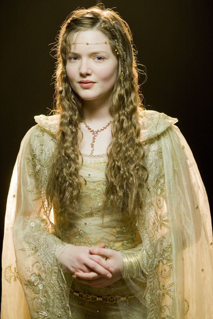 a young woman dressed in medieval clothing with long hair and wearing a crown, holding her hands on her chest