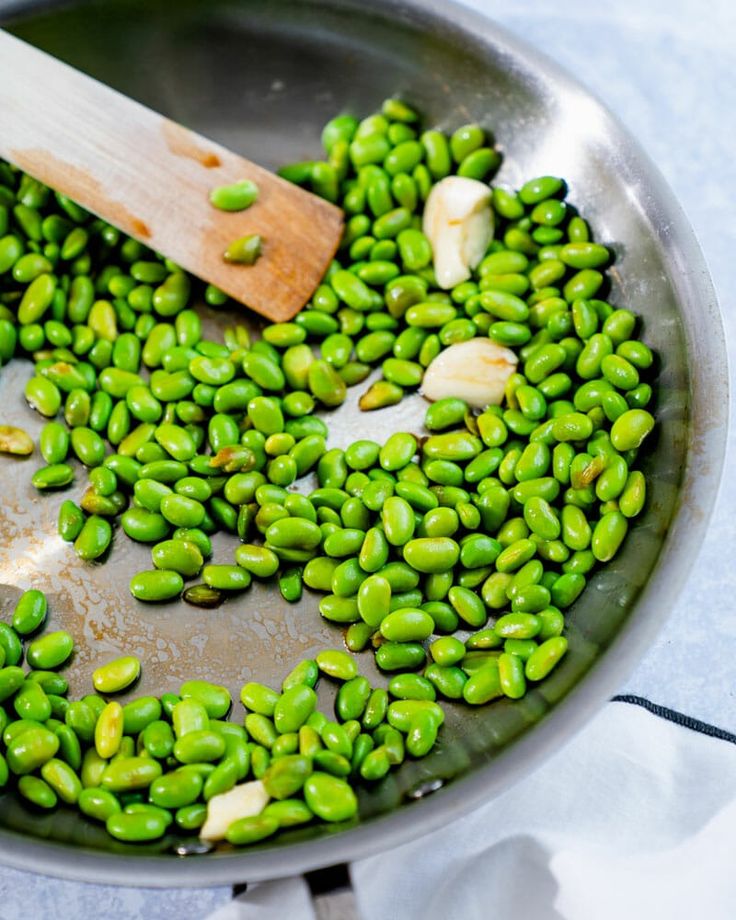 peas being cooked in a pan with a wooden spoon