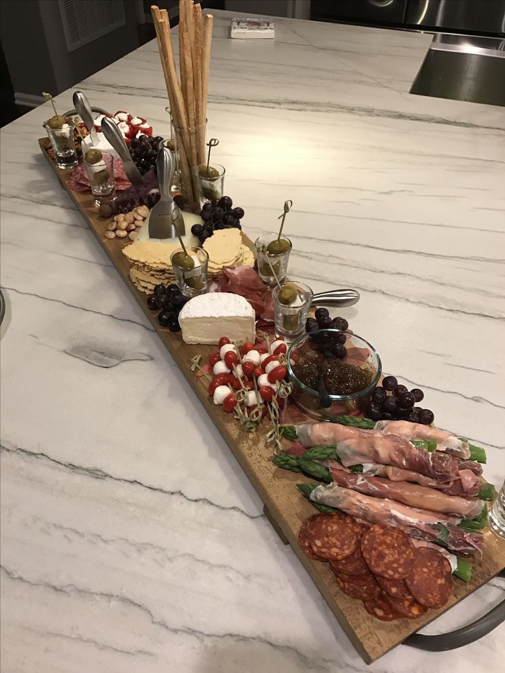 an assortment of meats and cheeses on a wooden platter sitting on a marble counter top