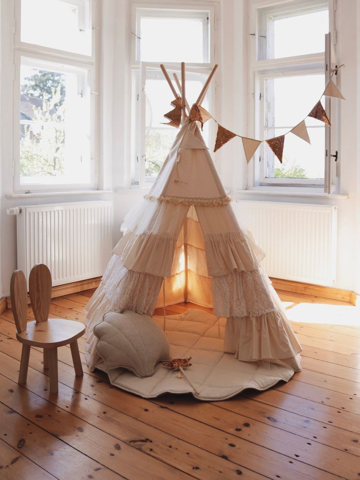 a teepee tent sitting on top of a wooden floor next to a chair and window