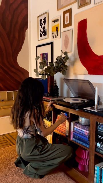 a woman sitting on the floor in front of a record player and bookshelf