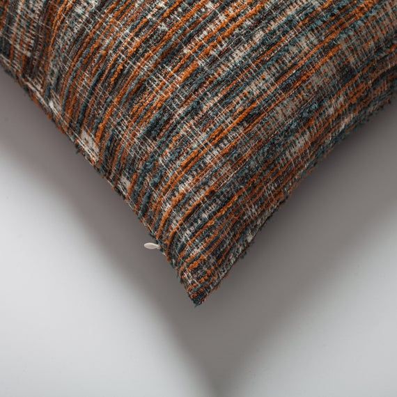 an orange, blue and grey pillow on a white surface with pins sticking out of it