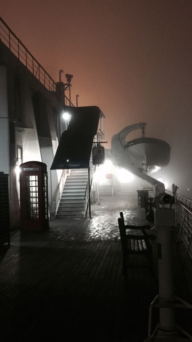 foggy night on the deck of a ship with stairs leading up to an open door