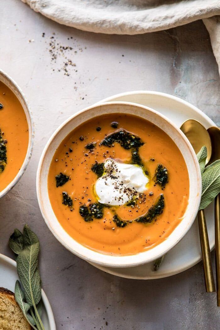 two bowls of carrot soup with bread on the side