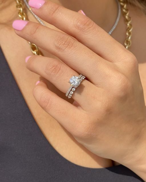 a woman's hand with pink and white manicured nails holding a diamond ring