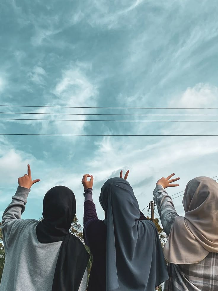 two women in hijabs are reaching up into the blue sky with their hands