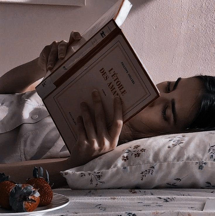 a woman laying in bed reading a book with strawberries on the table next to her