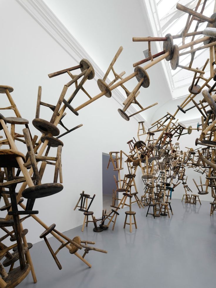 a room filled with lots of wooden chairs in it's walls and sculptures hanging from the ceiling