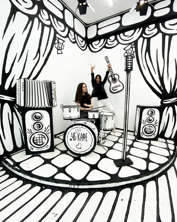 two women standing in front of an art installation with guitars and drums on the floor