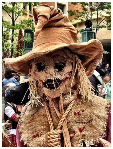 a scarecrow wearing a brown hat and holding a rope around his neck with other people in the background