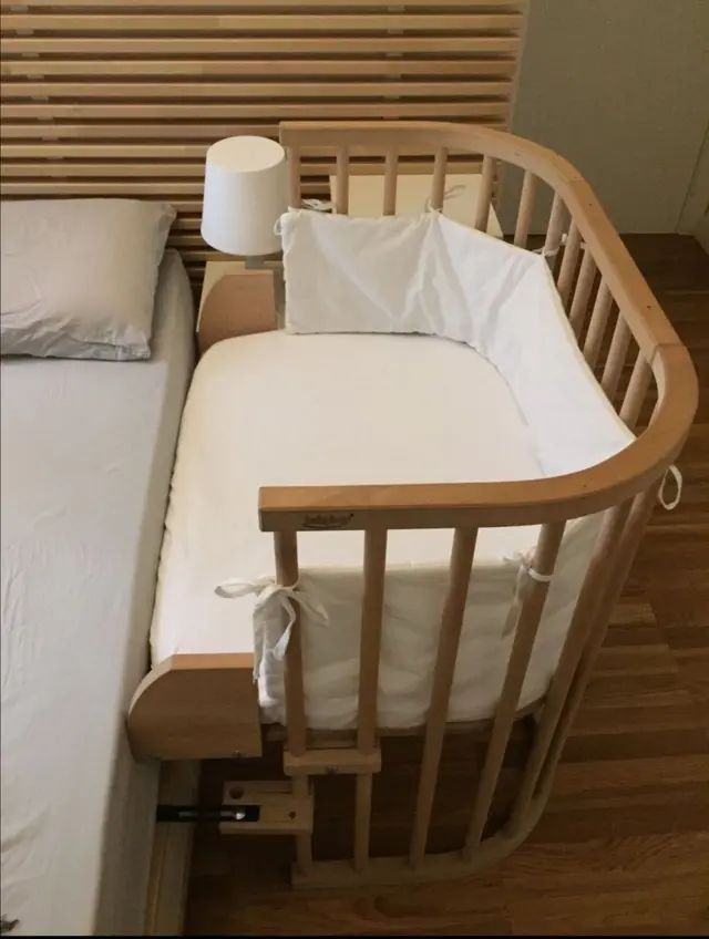 a small crib with two pillows and a pillow on the bottom bed, next to a night stand