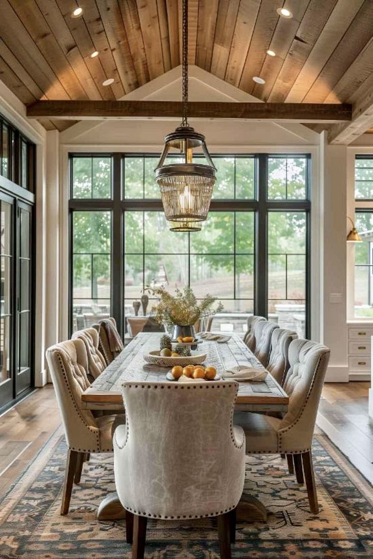 a dining room table with chairs and a chandelier hanging from the ceiling in front of large windows